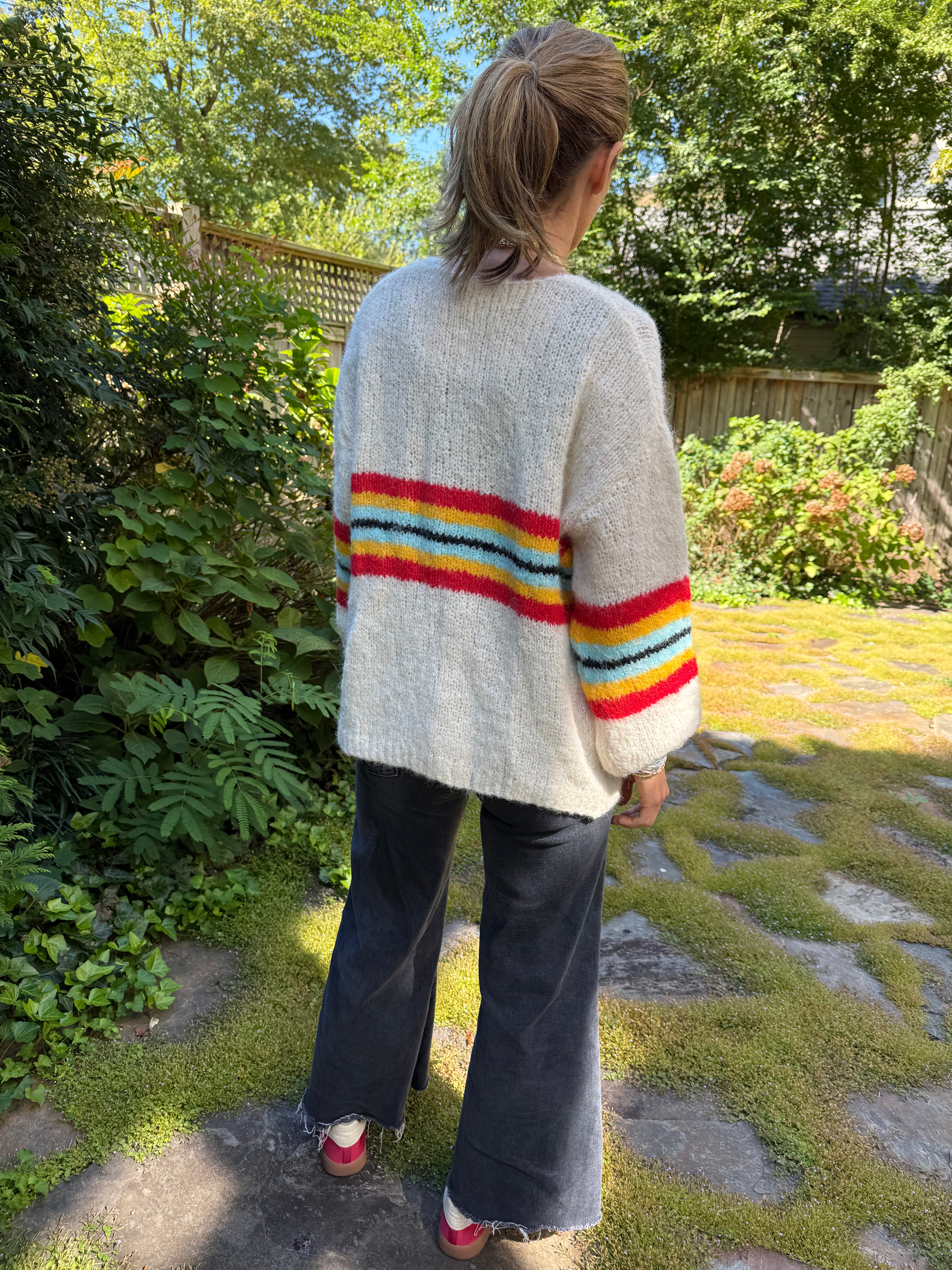 Person wearing a white sweater with a colorful striped design in a garden setting
