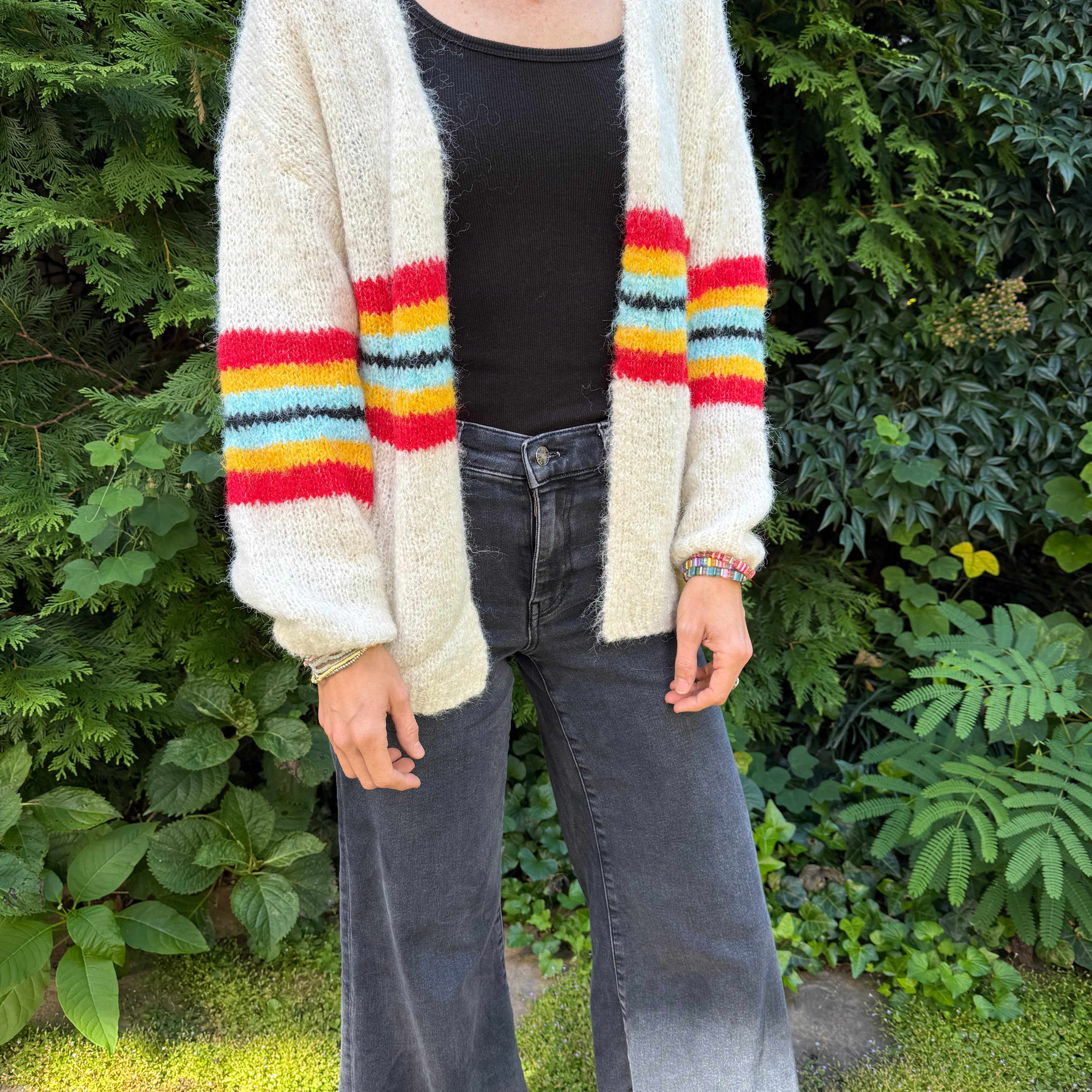Person wearing a cardigan with colorful stripes in front of green foliage