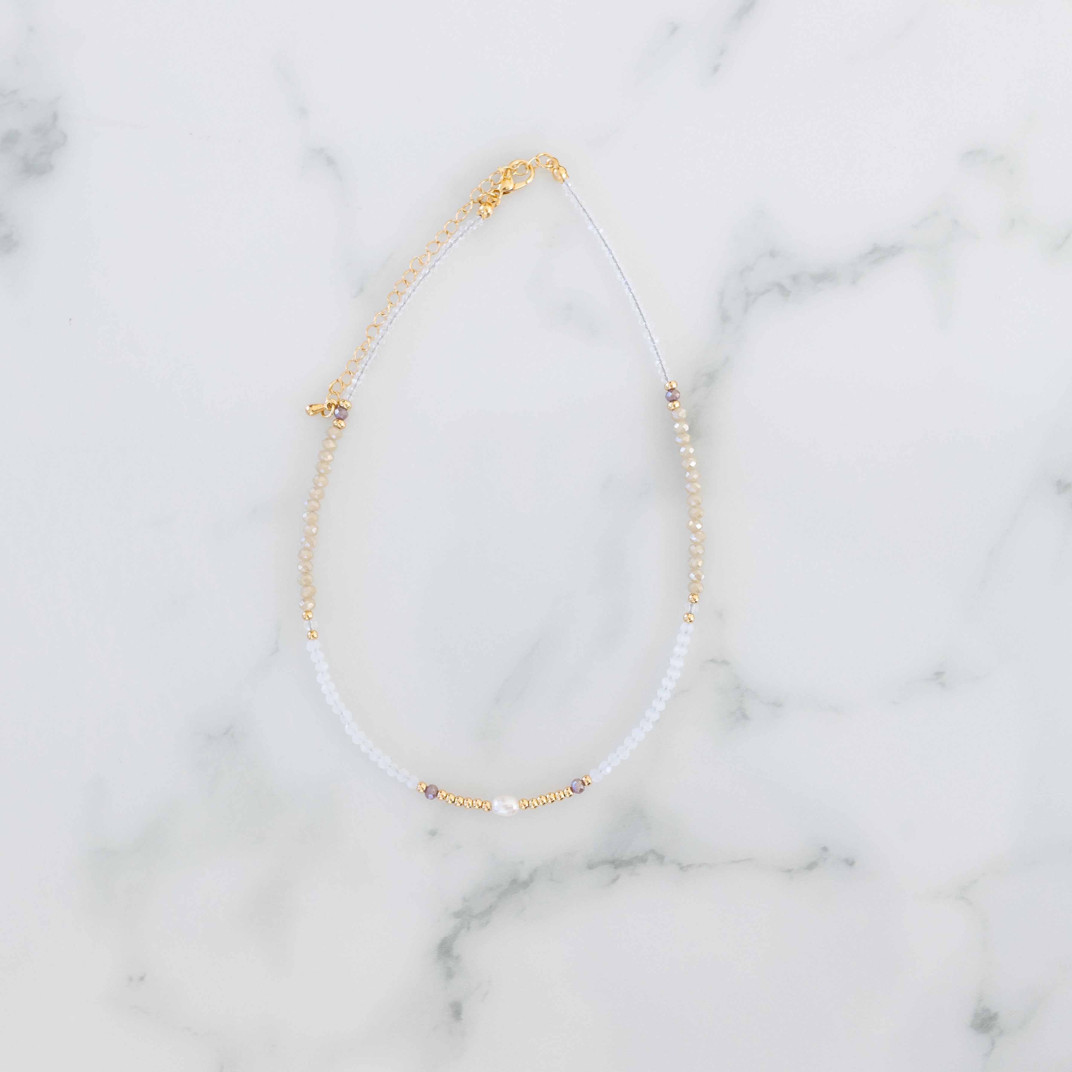 White and gold beads necklace on a marble background.