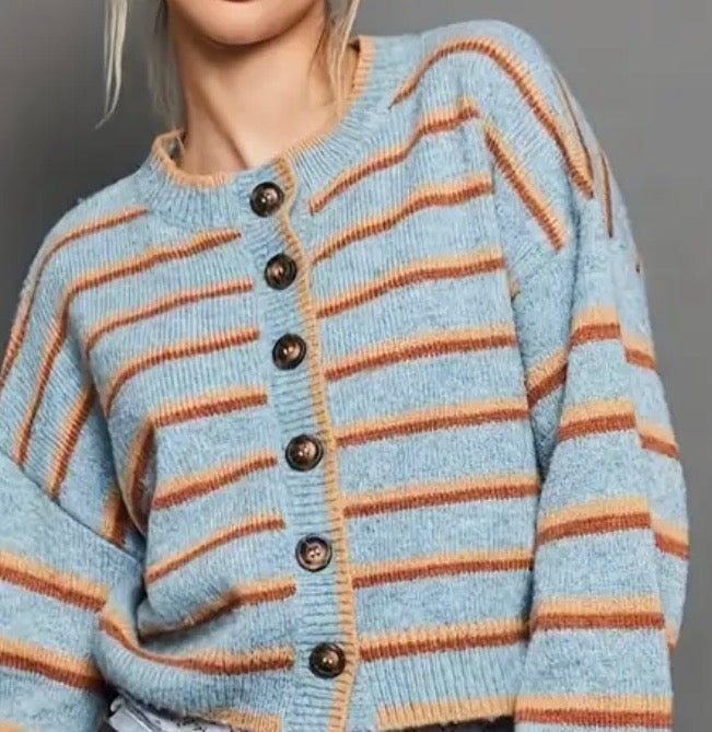 Light blue cardigan with orange and rust colored stripes and black buttons on a gray background