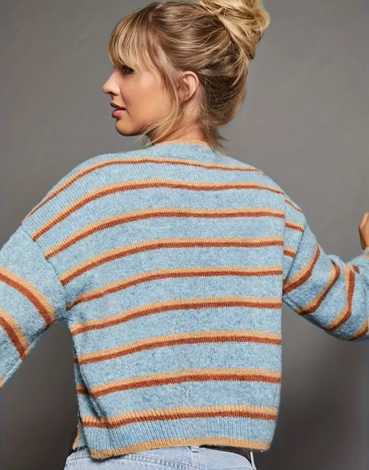 Light blue cardigan with orange and rust colored stripes and black buttons on a gray background