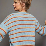 Light blue cardigan with orange and rust colored stripes and black buttons on a gray background