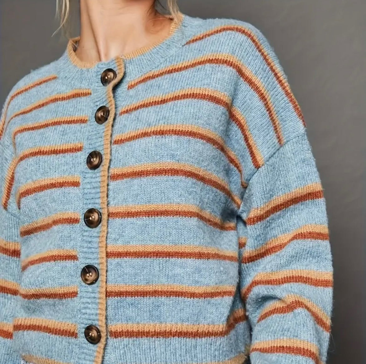 Light blue cardigan with orange and rust colored stripes and black buttons on a gray background