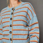 Light blue cardigan with orange and rust colored stripes and black buttons on a gray background