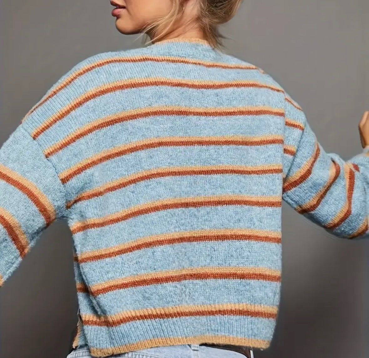 Light blue cardigan with orange and rust colored stripes and black buttons on a gray background