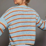Light blue cardigan with orange and rust colored stripes and black buttons on a gray background