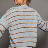 Light blue cardigan with orange and rust colored stripes and black buttons on a gray background