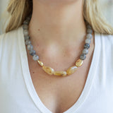 Necklace with gray and gold beads worn by a person in a white top