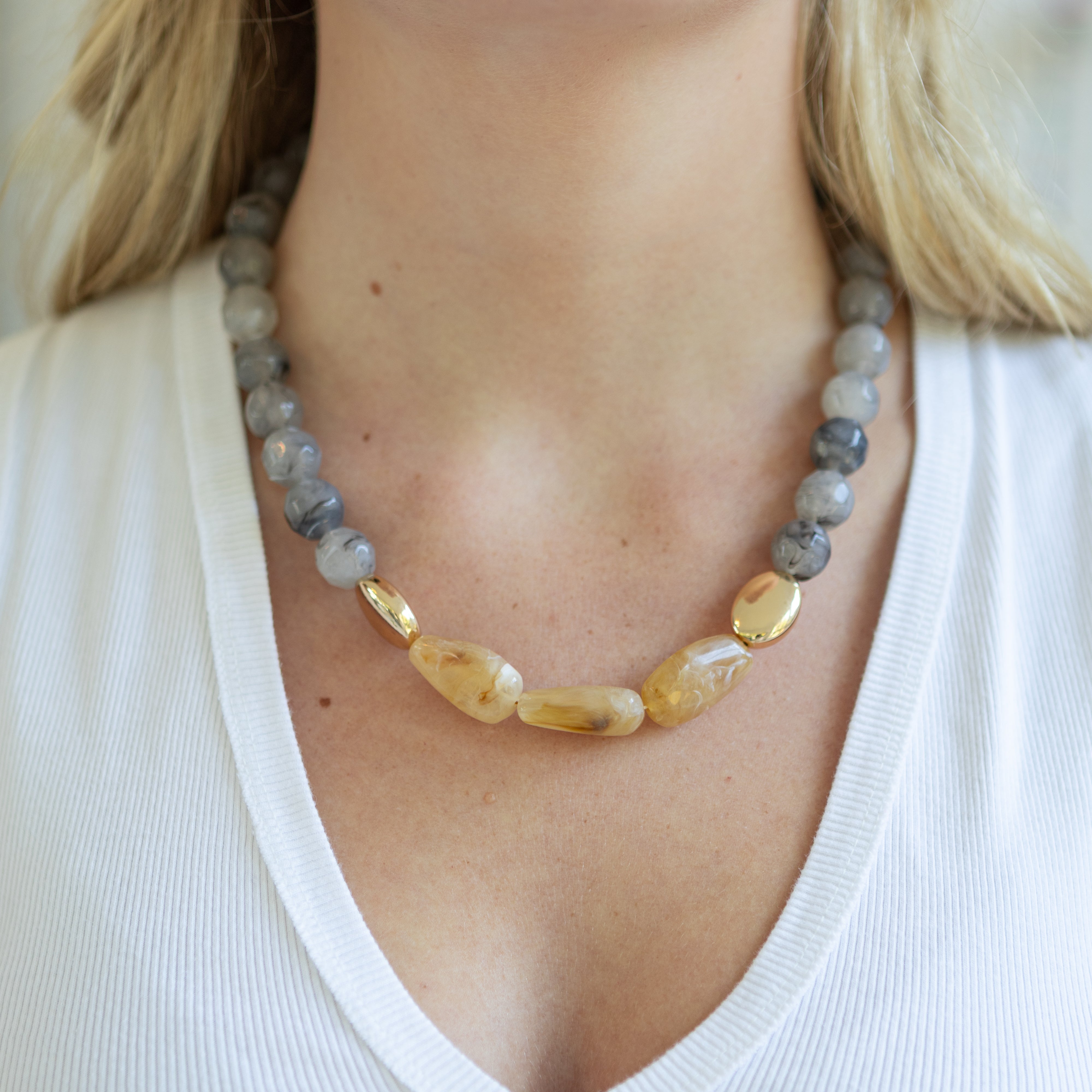 Necklace with gray and gold beads worn by a person in a white top