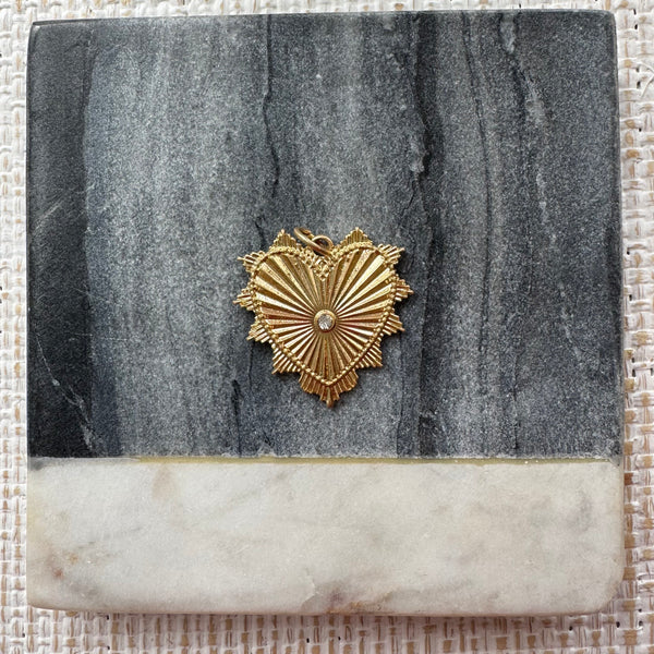 Gold heart pendant with a small clear stone at its center. Heart has an accordion texture and small triangles all around the edge.