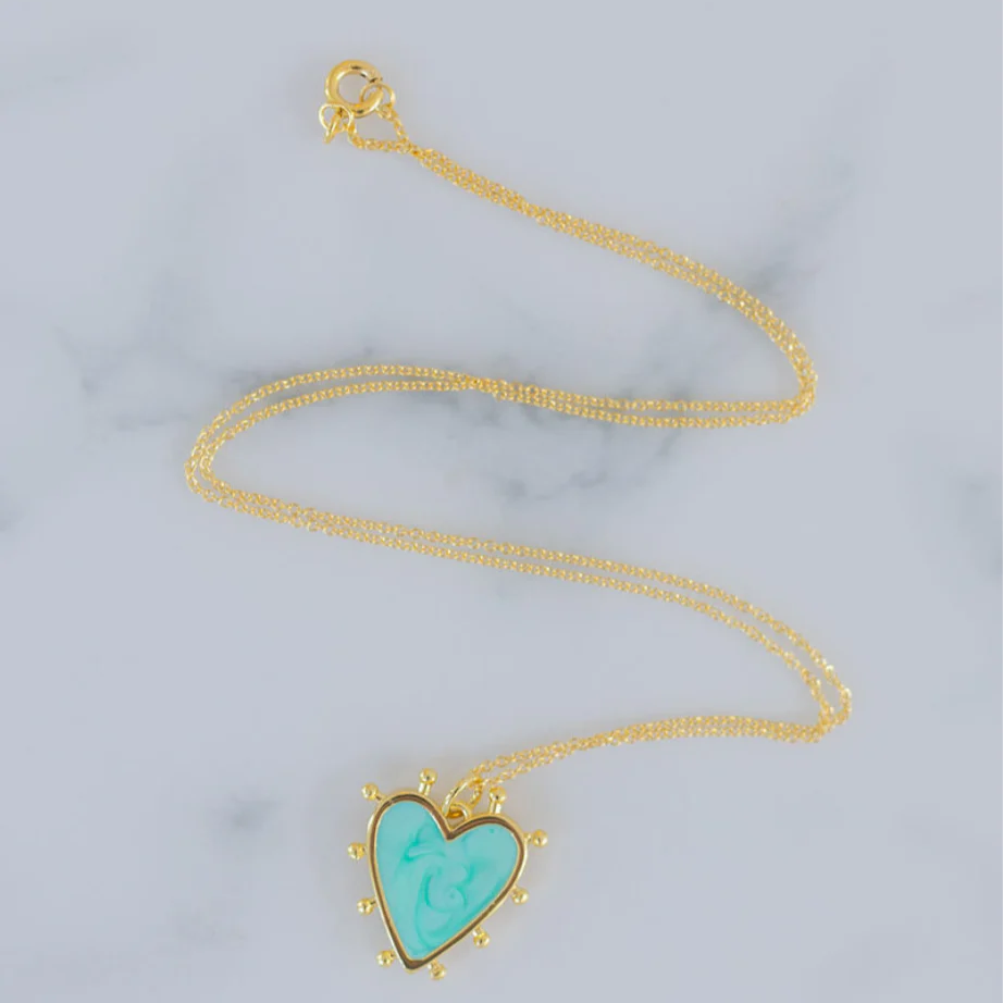 Delicate gold chain with a light blue heart enamel pendant that is edged in gold with small gold beads around its edges.
