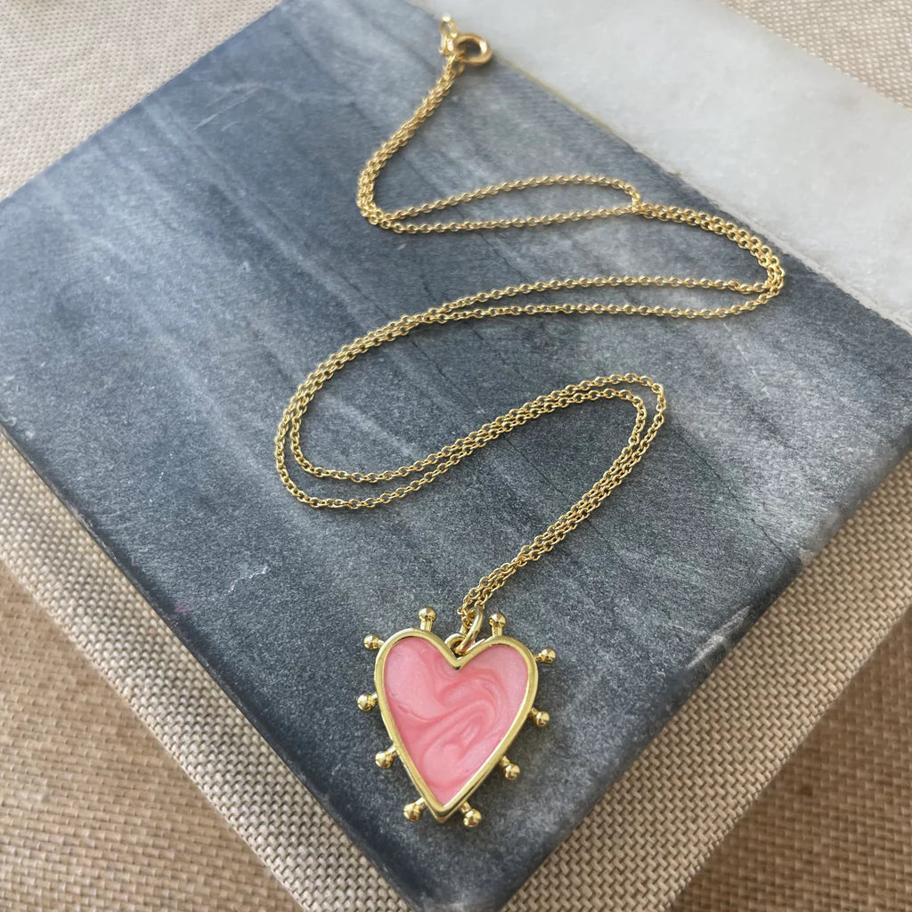 Delicate gold chain with a light pink heart enamel pendant that is edged in gold with small gold beads around its edges.
