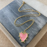 Delicate gold chain with a light pink heart enamel pendant that is edged in gold with small gold beads around its edges.